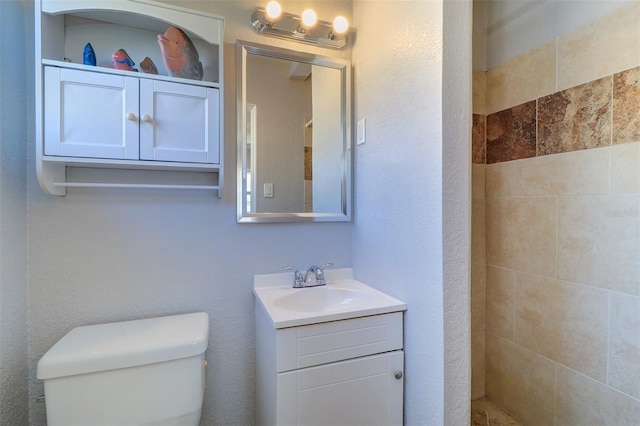 bathroom with toilet, tiled shower, and vanity