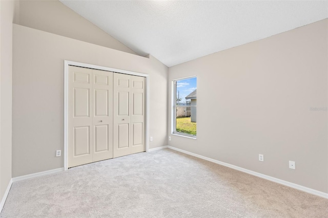 unfurnished bedroom featuring vaulted ceiling, light carpet, and a closet