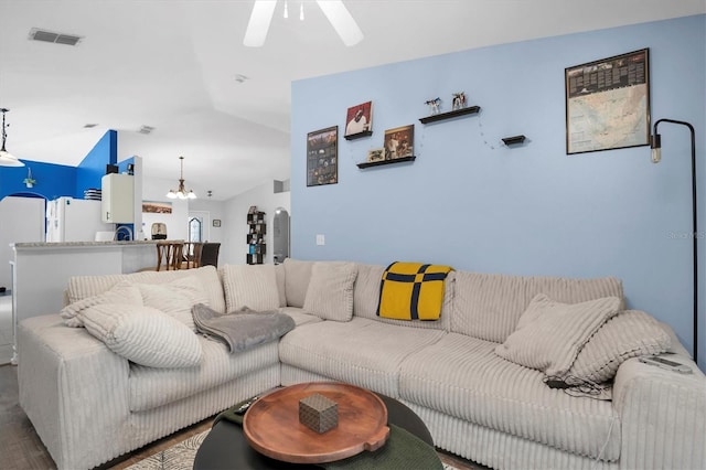 living room with ceiling fan with notable chandelier, hardwood / wood-style flooring, and vaulted ceiling