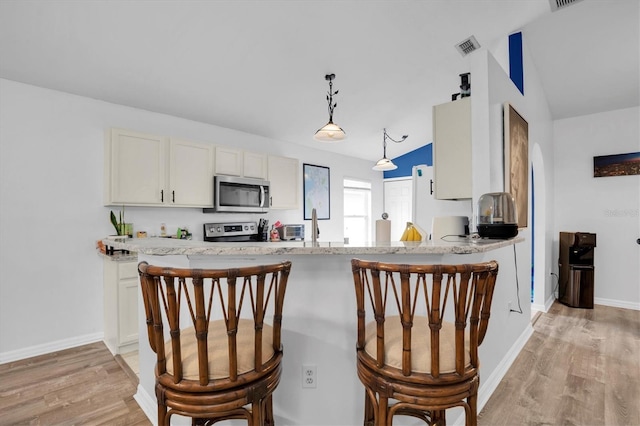 kitchen with appliances with stainless steel finishes, hanging light fixtures, kitchen peninsula, white cabinets, and lofted ceiling