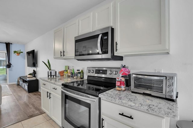 kitchen with stainless steel appliances, light tile patterned floors, light stone countertops, and white cabinets