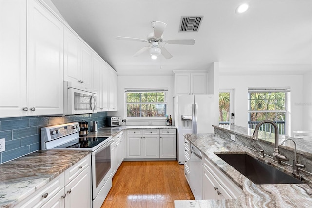 kitchen with sink, white appliances, white cabinetry, light stone countertops, and decorative backsplash