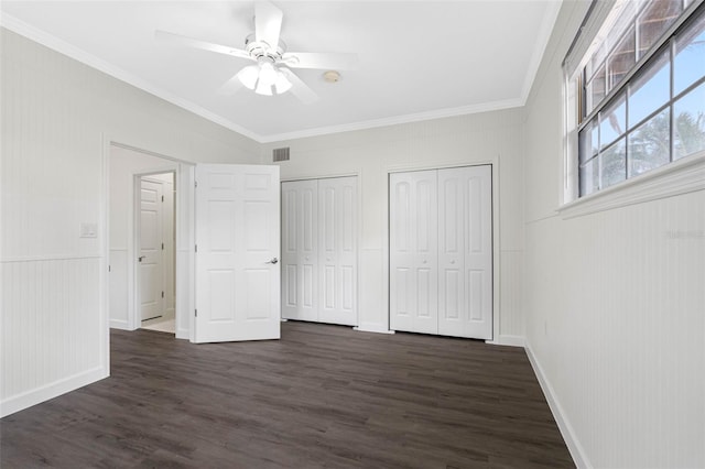 unfurnished bedroom featuring ceiling fan, ornamental molding, dark hardwood / wood-style floors, and two closets