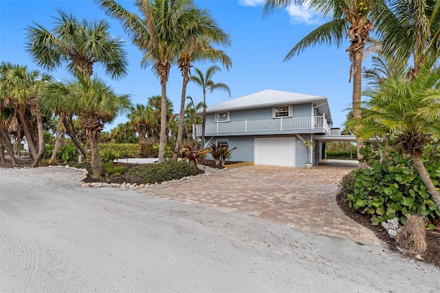 raised beach house with a carport, decorative driveway, a balcony, and an attached garage