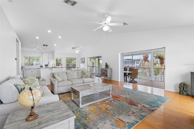 living area featuring visible vents, baseboards, light wood-style flooring, vaulted ceiling, and recessed lighting