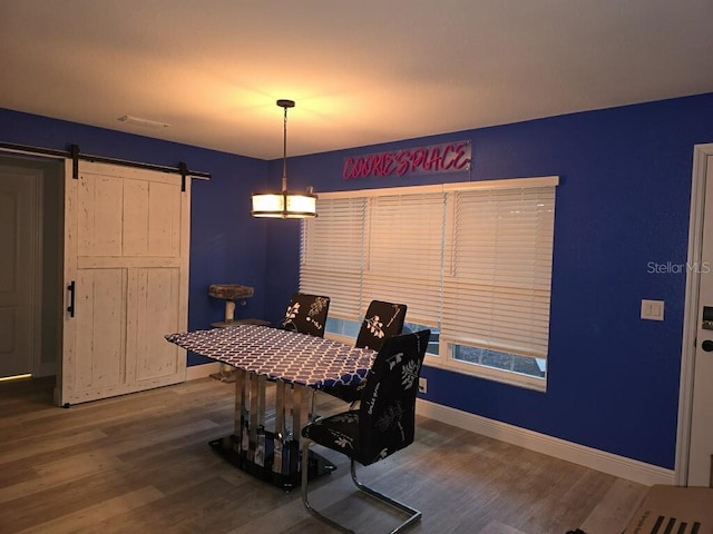 dining space featuring a barn door, an inviting chandelier, and hardwood / wood-style flooring