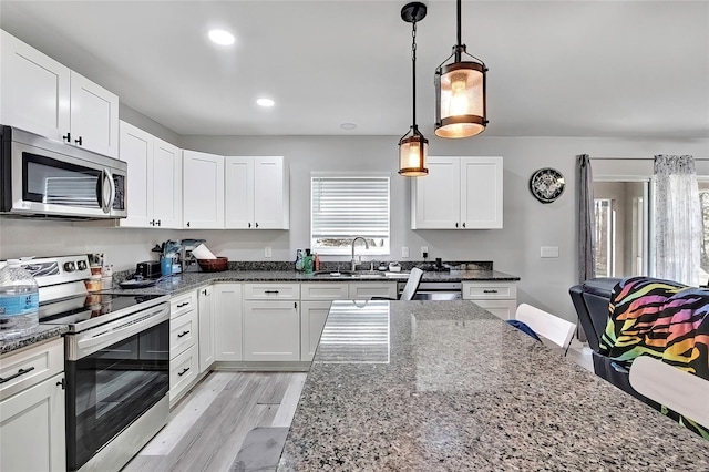 kitchen with dark stone counters, sink, hanging light fixtures, white cabinetry, and stainless steel appliances