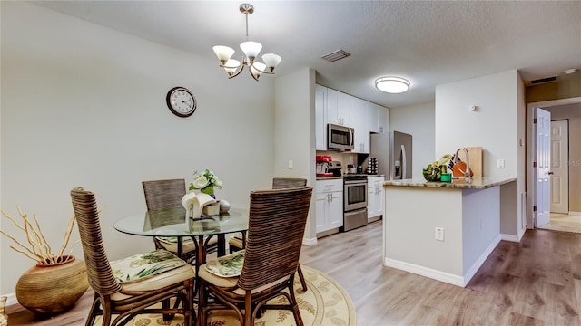 kitchen featuring stainless steel appliances, an inviting chandelier, light hardwood / wood-style flooring, pendant lighting, and white cabinets