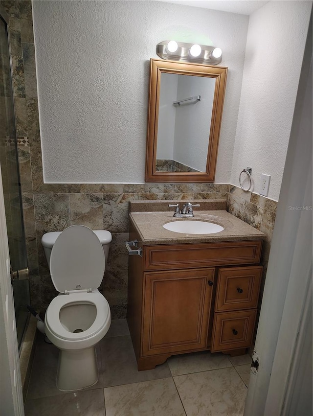 bathroom featuring tile patterned floors, vanity, tile walls, toilet, and walk in shower