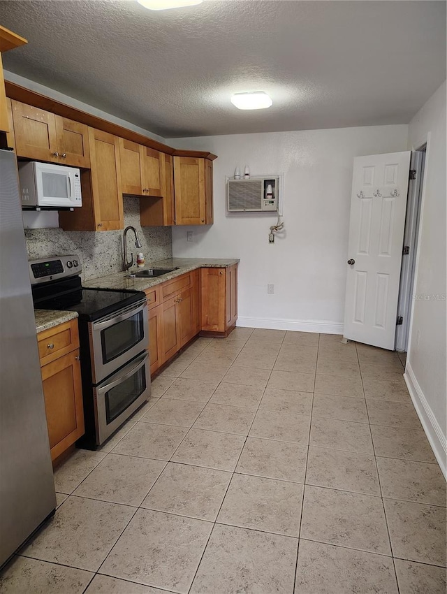 kitchen with a textured ceiling, appliances with stainless steel finishes, sink, light tile patterned floors, and a wall mounted air conditioner