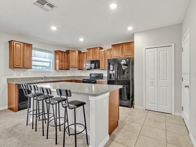 kitchen featuring a center island, black appliances, sink, light tile patterned floors, and a breakfast bar area