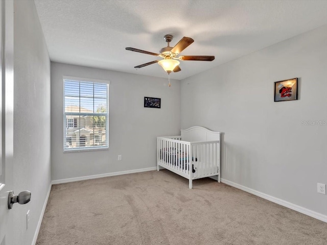 carpeted bedroom with ceiling fan and a nursery area