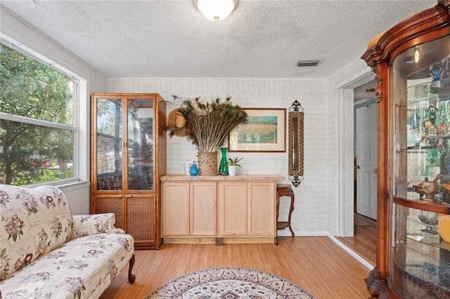 living area featuring a healthy amount of sunlight, a textured ceiling, brick wall, and light hardwood / wood-style flooring