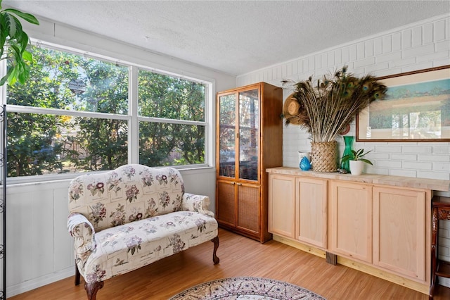 sitting room with a textured ceiling, a healthy amount of sunlight, brick wall, and light hardwood / wood-style floors