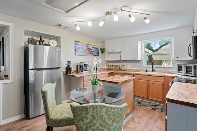 kitchen with butcher block counters, white cabinetry, sink, and stainless steel appliances