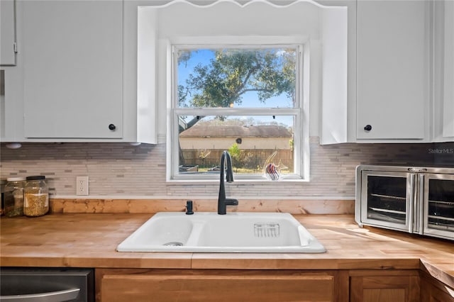 kitchen with stainless steel dishwasher, white cabinetry, butcher block counters, and sink