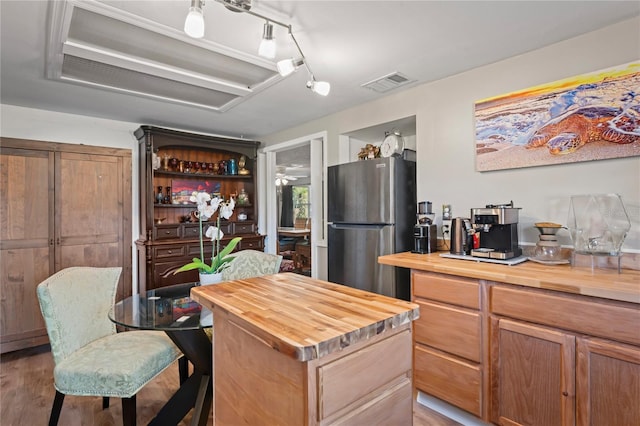 kitchen featuring wood counters, stainless steel fridge, ceiling fan, light hardwood / wood-style flooring, and a center island