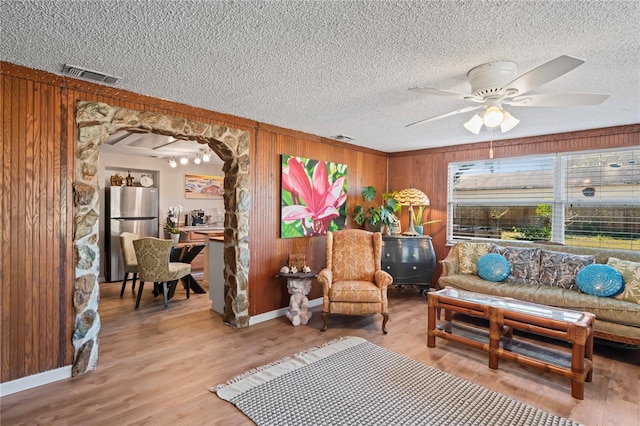 sitting room with ceiling fan, wood-type flooring, and wooden walls