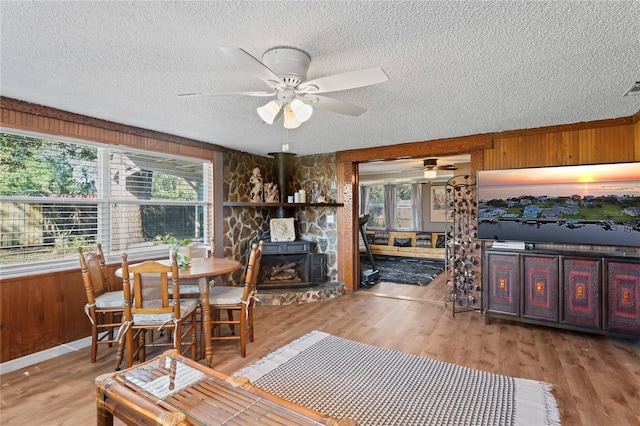 dining area featuring light hardwood / wood-style floors, ceiling fan, wood walls, and a wood stove