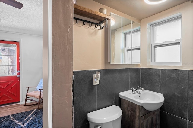 bathroom with wood-type flooring, a textured ceiling, toilet, vanity, and tile walls