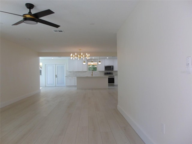 unfurnished living room featuring ceiling fan with notable chandelier and light wood-type flooring