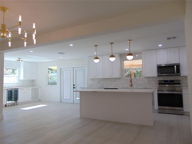 kitchen featuring stainless steel appliances, beverage cooler, decorative light fixtures, a chandelier, and white cabinetry