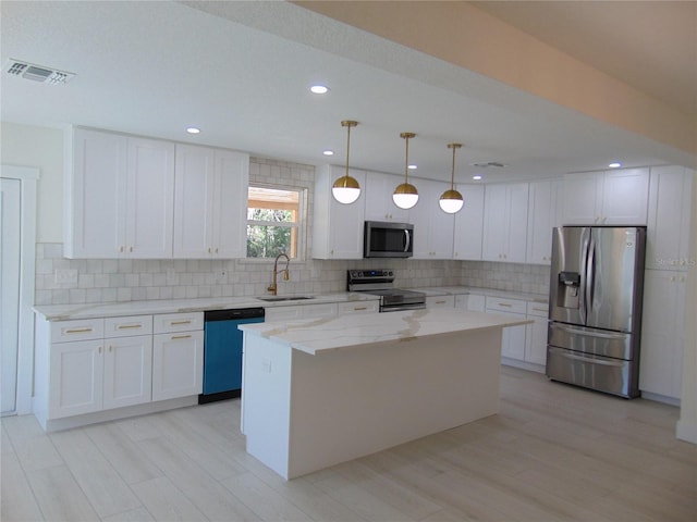 kitchen with appliances with stainless steel finishes, sink, white cabinets, a center island, and hanging light fixtures