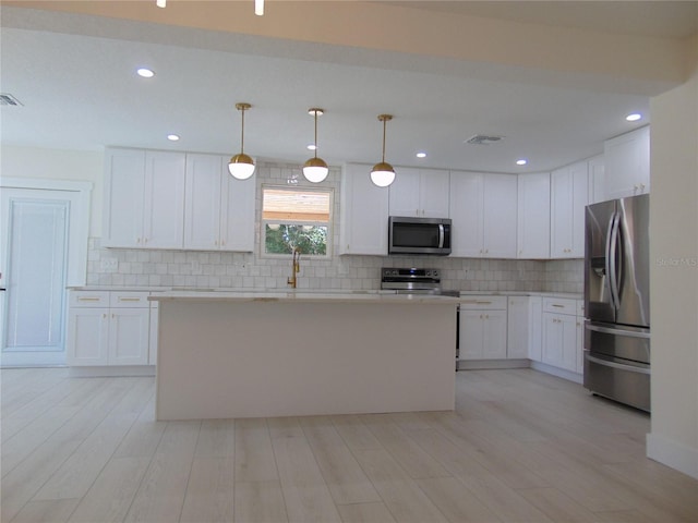 kitchen featuring a center island, stainless steel appliances, white cabinetry, and hanging light fixtures