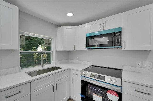 kitchen with stainless steel electric range oven, sink, white cabinets, and light stone counters