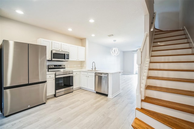 kitchen with sink, kitchen peninsula, decorative light fixtures, white cabinetry, and stainless steel appliances