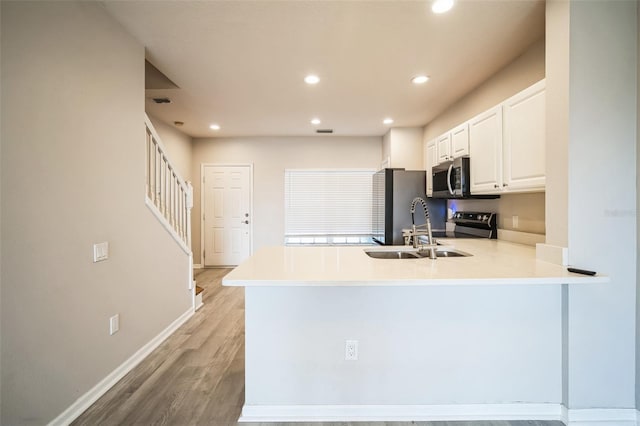 kitchen featuring white cabinetry, sink, kitchen peninsula, light hardwood / wood-style floors, and appliances with stainless steel finishes