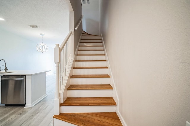 staircase with hardwood / wood-style floors, sink, and a textured ceiling