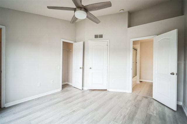 unfurnished bedroom featuring ensuite bath, ceiling fan, light hardwood / wood-style flooring, and a towering ceiling