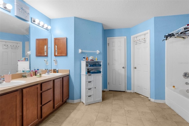 bathroom with a sink, baseboards, a textured ceiling, and double vanity