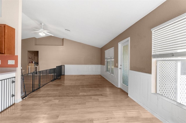 hallway with an upstairs landing, a wainscoted wall, light wood-style flooring, and vaulted ceiling