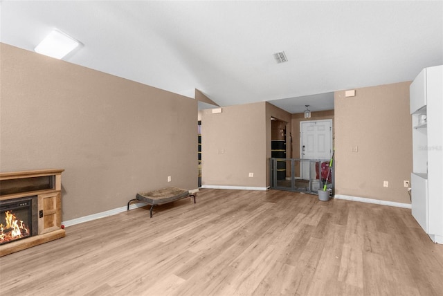 unfurnished living room featuring visible vents, baseboards, a lit fireplace, vaulted ceiling, and light wood-style floors