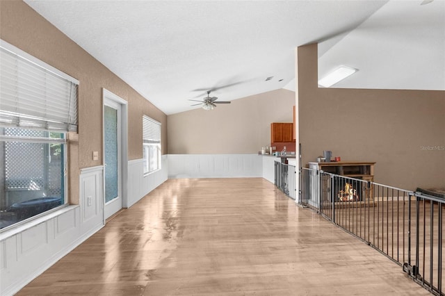 interior space featuring ceiling fan, a lit fireplace, lofted ceiling, wainscoting, and wood finished floors