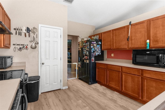 kitchen with black appliances, brown cabinetry, light countertops, and light wood-style floors