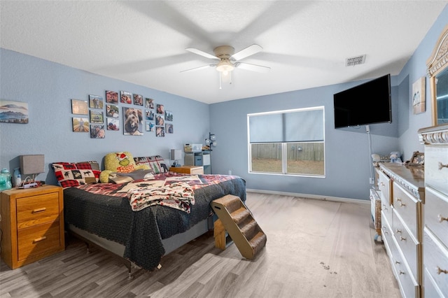 bedroom featuring visible vents, a textured ceiling, wood finished floors, baseboards, and ceiling fan