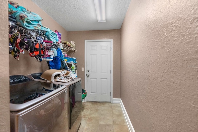 clothes washing area with baseboards, a textured wall, laundry area, a textured ceiling, and washing machine and dryer