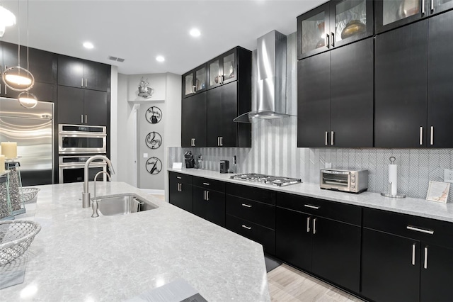 kitchen featuring decorative light fixtures, stainless steel appliances, sink, wall chimney range hood, and backsplash