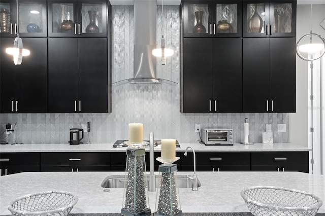 kitchen with stainless steel gas cooktop, wall chimney range hood, decorative light fixtures, and decorative backsplash