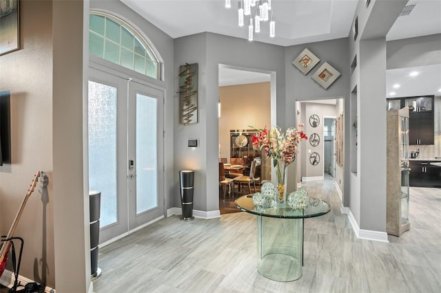 foyer featuring a healthy amount of sunlight, light hardwood / wood-style flooring, french doors, and an inviting chandelier