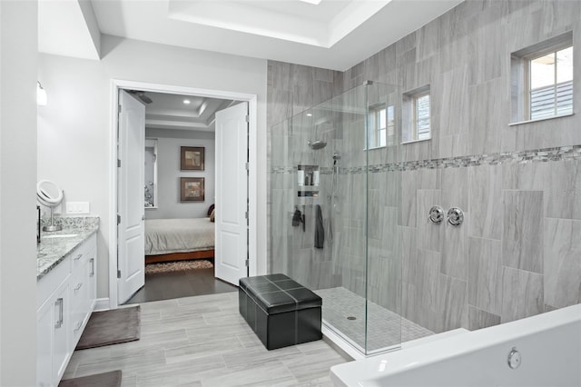 bathroom with a raised ceiling, a tile shower, and vanity