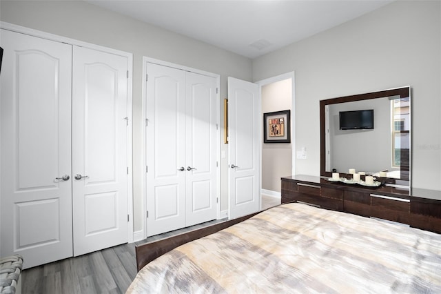 bedroom with radiator heating unit, two closets, and dark hardwood / wood-style floors