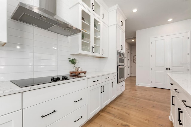 kitchen featuring wall chimney exhaust hood, white cabinetry, light stone countertops, and black electric cooktop