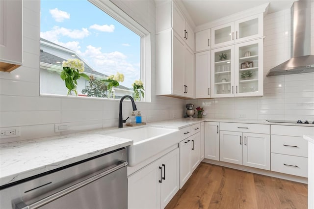 kitchen featuring stainless steel dishwasher, wall chimney exhaust hood, white cabinets, and sink