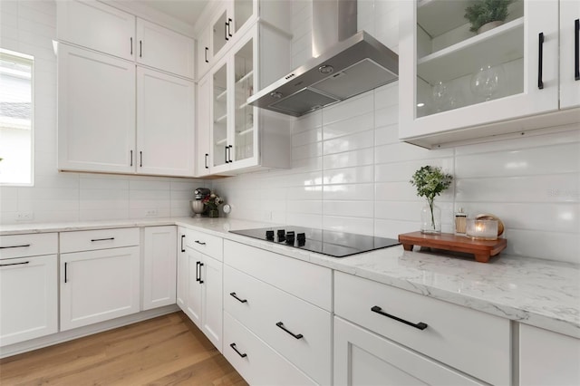 kitchen with backsplash, black electric cooktop, wall chimney range hood, light hardwood / wood-style floors, and white cabinetry