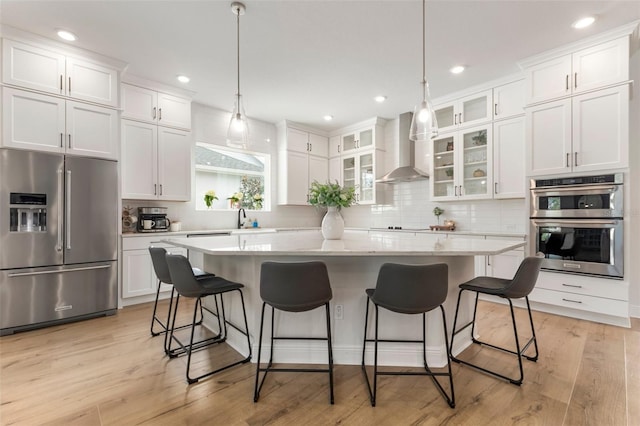 kitchen with white cabinetry, wall chimney range hood, light hardwood / wood-style floors, a kitchen island, and appliances with stainless steel finishes