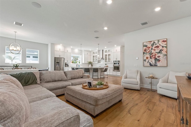 living room with a notable chandelier, light hardwood / wood-style floors, and sink